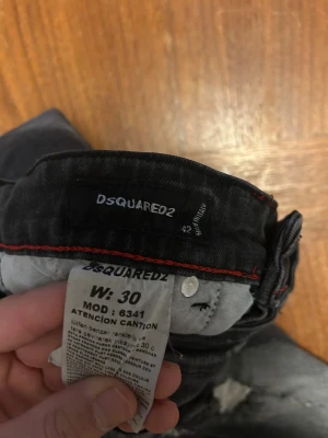 Svarta skinny jeans från Dsquared2 - Snygga svarta skinny jeans från Dsquared2 med slitna detaljer och coola slitningar framtill. Jeansen har en smal passform, klassisk femficksdesign och röda sömmar på insidan av linningen. Perfekta för dig som gillar en edgy streetstil.