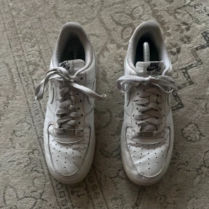 Nike Air Force 1 vita sneakers - Klassiska Nike Air Force 1 sneakers i helvitt skinn med perforerad tå, rund tå och platt sula. Skorna har snörning och den ikoniska Nike-loggan på sidan och hälen. Perfekt för dig som gillar en clean och tidlös streetstil. Som nya kostar d runt 1000kr så d är ett rätt så bra pris!!