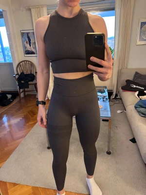 Mörkgrå ribbade leggings från Stronger - Säljer ett par mörkgrå ribbade leggings samt topp från Stronger i storlek XS/S . De är högmidjade och har en tight passform som sitter snyggt. Säljs tillsammans för 150kr eller 100kr var för sig!