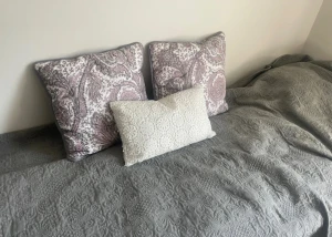 Elegant bäddset från Mio – överkast + kuddar - Säljer ett vackert och stilrent set som skapar hotellkänsla i sovrummet: 	•	Sängöverkast från Mio, 180 cm brett – dovt grått med vackert strukturmönster i hög kvalitet. 	•	2 rosa paisleymönstrade prydnadskuddar från Mio – stora, lyxiga och i mycket fint skick. 	•	1 vit avlång kudde med vackert spetsbroderi – perfekt som kontrast. Innekuddar ingår ej Skick: Väldigt fint, endast använt i gästrum. 