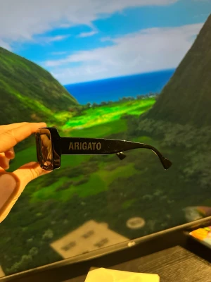 Svarta Axel Arigato solglasögon - Snygga svarta solglasögon från Axel Arigato med rektangulär form och breda skalmar där loggan är tryckt i silver. Glasögonen kommer med ett beige fodral i skinn med knappstängning. Perfekt accessoar för en cool look.