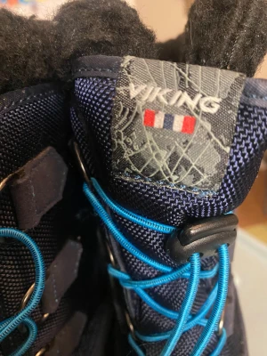 Viking vinterstövlar med blå snörning - Säljer ett par mörkblå vinterstövlar från Viking med grov sula och blå snörning. Ovandelen är i slitstark syntet och nederdelen i svart gummi, med mjukt svart foder upptill. Perfekt för kalla dagar och snö. De är aldrig använda då de var fel storlek under vintersäsongen.