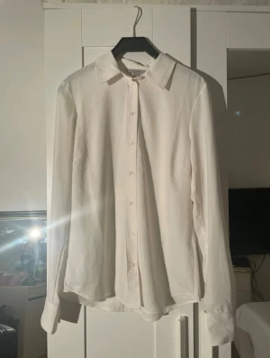Vit klassisk skjorta från H&M - Vit skjorta från H&M i storlek XS med klassisk krage och knappar hela vägen framtill. Skjortan har lång ärm och är tillverkad i mjukt bomullsmaterial.