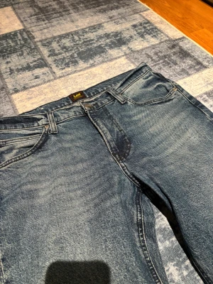 Blå raka jeans från Lee - Bå jeans från Lee med raka ben och normal passform. Jeansen har använts ett fåtal gånger, och är näst in till i ny skick. Jeansen är tillverkade i slitstarkt denimtyg av bomull. 