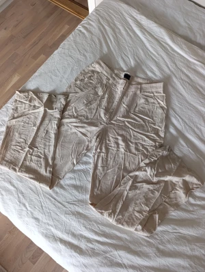 Beiga linnebyxor från ASOS Design TALL - Snygga beiga linnebyxor från ASOS Design TALL i rak passform. Byxorna har hög midja, bälteshällor och stängs med knapp och dragkedja. Materialet är en mix av viskos och linne, vilket ger en luftig och skön känsla.