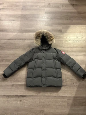 Canada Goose jacka  - Mörkgrå dunjacka från Canada Goose  Säljer min Canada Goose-jacka i mörkgrått, komplett med päls på huvan. Den är riktigt varm och perfekt för vintern. Jackan är i väldigt bra skick och har alltid tagits väl hand om. Det enda som finns att anmärka på är ett litet märke på baksidan (syns på bild 7),men det är inget som stör eller påverkar funktionen. Det här är en kvalitetsjacka som håller värmen ordentligt och perfekt jacka för vinter. Väldigt skön att ha på sig och sitter riktigt bekvämt  Pris 
