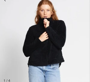 Svart teddyjacka från 157 - Mjuk och fluffig svart teddyjacka med hel dragkedja och hög krage. Jackan har en loose passform och är perfekt för kyliga dagar. Materialet är fleece och ger en skön och avslappnad vibe. Snygg att styla med jeans eller mjukisbyxor.