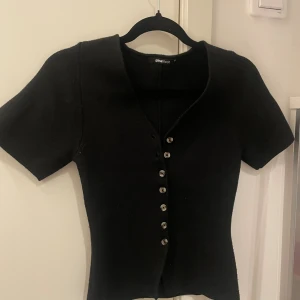Svart stickad topp från Gina Tricot - Snygg svart stickad topp från Gina Tricot med korta ärmar och v-ringning.Sitter jätte snyggt på och formar.