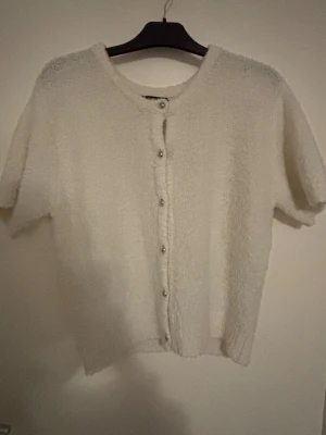 Vit fluffig kofta med kort ärm - Supermysig vit kofta med korta ärmar och fluffig textur. Koftan har rund hals och knäpps med små silvriga knappar framtill. Perfekt för att ge din outfit en soft och chill vibe. Endast använd en gång. Storlek L. Hör av dig via e-mejl eller mobilnummer då jag inte kan ta emot Swish på detta nummer. E-mejl emli.com@icloud.com mobil-0728875624 mvh Emilia/marina😊