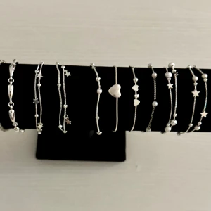Mix av silver- och guldfärgade armband - Säljer ett gäng snygga armband i både silver och guld. Flera har detaljer som små stjärnor, hjärtan och pärlor, samt ett med årtalet 2009. Några är kedjeformade, andra har vågig eller texturerad design. Perfekt för att skapa din egen coola look med olika stilar och former.styck pris 100/150kr