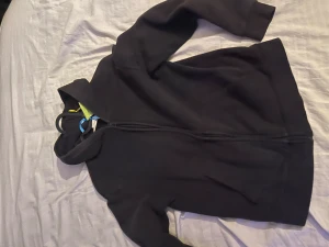 Svart hoodie med dragkedja - Svart hoodie med hel dragkedja framtill och huva. Tröjan har långa ärmar och två fickor på sidorna. Perfekt för chill dagar eller när du vill ha en enkel och stilren look. Materialet känns mjukt och bekvämt mot huden.