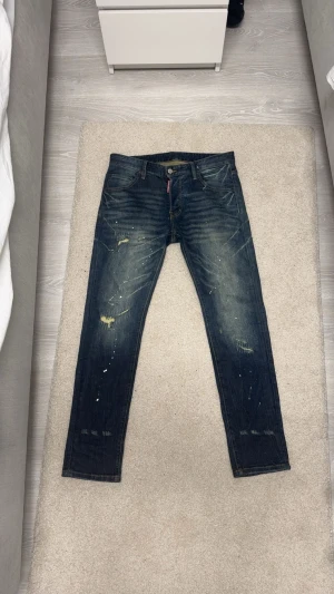 Dsquared2  - Snygga blå jeans, Dsquared2 med coola färgstänk och slitningar för en edgy look. Klassisk femficksmodell med Dsquared2-logga på både etikett och knapp. Jeansen har en rak passform och är tillverkade i robust denim.