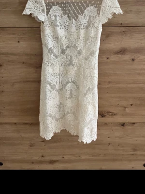 Vit idasjöstet klänning - Supersöt vit kortklänning i spets med fina detaljer och korta ärmar. Klänningen har ett romantiskt mönster och transparent parti upptill som ger en extra touch. Perfekt för sommarens alla tillfällen!dock har den missfärgningar lite här och var