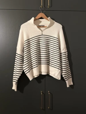 Randig stickad half zip tröja - Säljer en vit och svart randig stickad tröja från Mango. Tröjan har en relaxed passform, lång ärm och en snygg half zip-dragkedja vid kragen. Perfekt till höst och vår för en chill look. Använd 3-4 gånger endast!