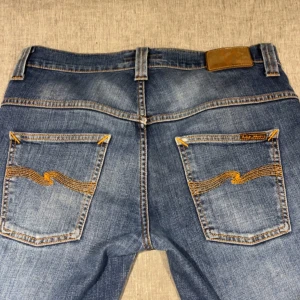 Blå jeans från Nudie Jeans Co W30 L32 - Säljer ett par klassiska blå jeans från Nudie Jeans. Modellen har raka ben, fem fickor och coola detaljer på bakfickorna. Perfekta för dig som är grish men ändå vill sticka ut lite. Priset kan diskuteras.