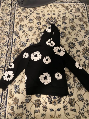 Denim tears hoodie - En fin tröja som är svart met blommor på den är i nu skick och ser bra ut på en och den är varm så en bra tröja för vintern