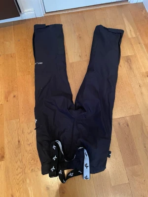 Svarta täckbyxor Cross Sportswear XS - Svarta täckbyxor från Cross Sportswear i storlek XS. Byxorna har justerbara hängslen med logga, dragkedjor vid fickorna och stängs med både knapp och kardborre. Perfekta för vinterns alla äventyr och håller dig torr och varm.