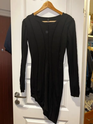 Svart asymmetrisk klänning från SHEIN - Säljer en svart ribbad klänning från SHEIN i storlek M. Klänningen har lång ärm och en cool asymmetrisk nederkant som ger en edgy vibe. Materialet är stretchigt och figurnära, perfekt för dig som gillar en slim passform.