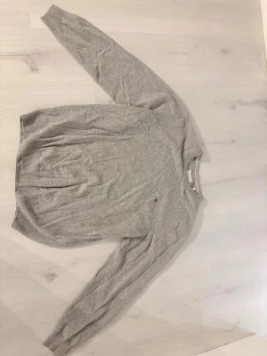 Ljusgrå ulltröja från GANT - Säljer en ljusgrå stickad tröja från GANT i superfin lammull. Klassisk rund halsringning och diskret logga broderad på bröstet. Perfekt för dig som gillar stilrena och bekväma plagg med premiumkänsla.