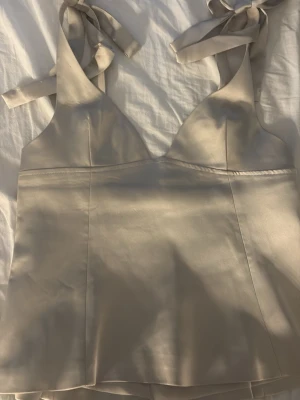 Champagnefärgad satinlinnetopp Gina Tricot - Säljer en champagnefärgad linnetopp från Gina Tricot i glansig satin. Toppen har breda axelband som knyts till rosetter på axlarna och en snygg v-ringad skärning. Perfekt att styla med jeans eller kjol för en trendig look. 