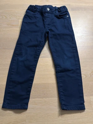 Mörkblå chinos från LC Waikiki - Snygga mörkblå chinos från LC Waikiki i mjuk bomull. Klassisk rak passform med knapp och hällor för bälte. Perfekta till vardags och lätta att matcha med olika tröjor. Passar barn i storlek 3-4 år.