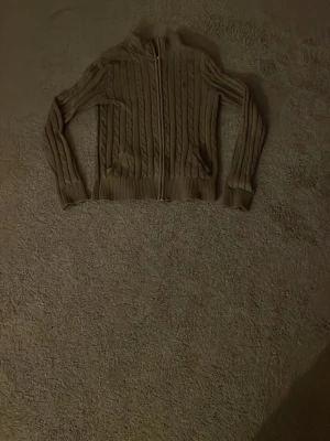 Mörkgrå kabelstickad kofta med dragkedja - Säljer en grå kabelstickad kofta med dragkedja framtill. Tröjan har lång ärm, ribbade muddar och hög krage. Perfekt för lager på lager och ger en klassisk look med sitt stickade mönster. Tröjan saknar tyvär drag grejen på drag kedjan men det är enkelt att reparera nypris 2500. 