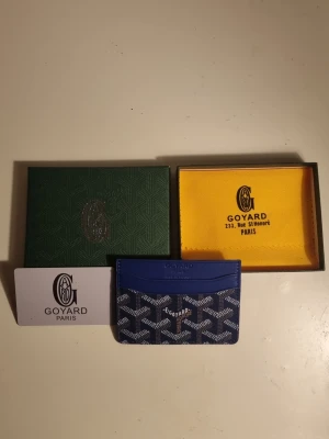 Blå Goy4ard plånbok med mönster - Säljer en blå Goy4ard plånbok i klassisk design med ikoniskt vitt och svart mönster. Plånboken har flera kortfack och är tillverkad i skinn med Goy4ards signaturtryck. Kommer med original ask och dustbag. Perfekt för dig som vill ha något unikt och stilrent.