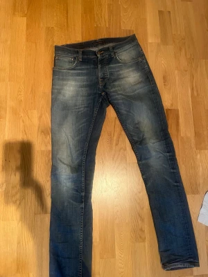 Nudie Jeans Grim Tim - Säljer ett par blå Nudie Jeans Grim Tim Worn in Broken i storlek 30/34. Jeansen har klassisk femficksdesign, raka ben och slitningar för en cool look. Materialet är 98% bomull och 2% elastan för skön stretch. Perfekta för dig som gillar en avslappnad stil.