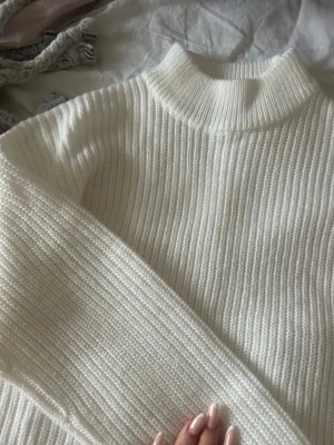 Vit ribbad stickad polotröja - Säljer en vit ribbad stickad polotröja med hög hals och lång ärm. Tröjan har en clean och enkel look, perfekt för lager på lager under höst och vinter. Mjuk och skön kvalitet som håller dig varm och snygg. Storlek XXS men passar XS. Aldrig använt