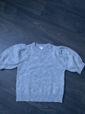 Grå stickad tröja Gina Tricot -  Fin grå stickad tröja från Gina Tricot med puffärmar och ribbade muddar. Säljer för använder aldrig.
