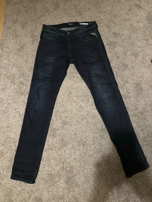 Replay Anbass Jeans blå - Säljer ett par mörkblå Replay Anbass slim fit jeans. Jeansen har snygga kontrastsömmar, läderpatch bak och diskret Replay-logga på fickan. Materialet är mjukt jeans-tyg som sitter tajt men ändå bekvämt. nypris runt 1000kr