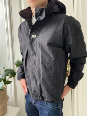 Helly Hansen - Helly Hansen regnjacka / vindjacka. Den är väldigt stor på modellen som är 180 cm 75 kg och bär M/M. Den klassiska helly Hansen regnjacka / vindjacka. Med HH loggan omkring jackan. Inga defekter på jackan - en väldigt trevlig jacka som passar perfekt för vintern och våren. 