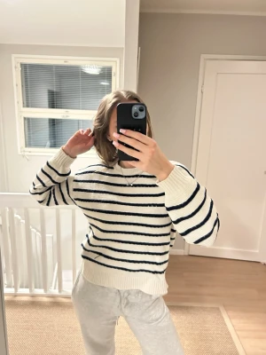 Randig stickad tröja i vitt och marinblått - Säljer en mysig stickad tröja med vita och marinblå ränder. Tröjan har rund hals, ribbade muddar och en relaxed passform. Perfekt för lager-på-lager och chill dagar. Passar både till jeans och mjukisbyxor.