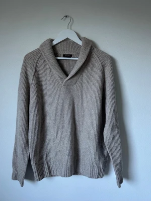 Beige ribbad ulltröja Massimo Dutti - Säljer en beige ribbstickad tröja från Massimo Dutti i 100% ull. Tröjan har en bred krage och lång ärm, perfekt för kyliga dagar. Enkel men stilren design som funkar till allt. Snyggt oversized fit och riktigt mjuk känsla. 6R1
