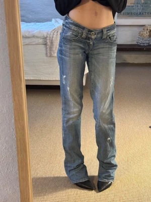 Blå raka jeans från Guess - Säljer ett par snygga raka jeans i ljusblå tvätt från Guess med låg midja och slitna detaljer. Jeansen är i storlek 24. Passar både storlek 32 och 34.