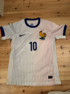  Frankrike fotbollströja Mbappé - Säljer en Frankrike fotbollströja från Nike med Mbappé och nummer 10 på ryggen. Tröjan är vit med tunna blå och röda ränder, blå detaljer vid krage och ärmslut samt broderad tupp på bröstet. Tillverkad i lätt polyester för bästa komfort på planen.🚨 Den är i Stolek S⚡️ Vid frågor hör av dig‼️