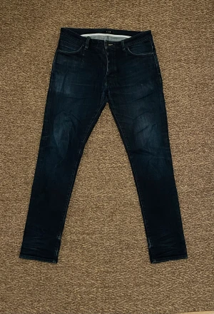 Mörkblå  jeans Nuew - Snygga mörkblå jeans från Nuew med klassisk femficksdesign. Jeansen har en skinny siluett, normal midja och är tillverkade i stretchigt denim för extra komfort. Perfekt för dig som gillar en stilren och modern look.