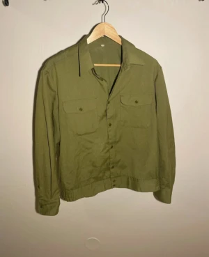 Olivgrön overshirt med fickor - Olivgrön overshirt i bomull med klassisk krage och två bröstfickor med lock och knappar. Långärmad modell med knäppning framtill och enkel, rak passform. Perfekt för lager-på-lager och snygg till jeans.