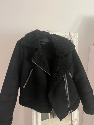 Svart teddyjacka - Säljer en svart teddyjacka från stradivarius med bred krage och synliga dragkedjor. Jackan har mjukt teddyfoder, croppad passform och detaljer i syntetmaterial. Perfekt för dig som gillar en cool och mysig look med extra edge.