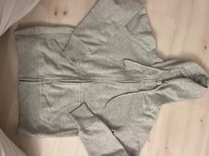 Grå hoodie med dragkedja och huva - Snygg grå hoodie i storlek S. Tröjan har hel dragkedja framtill, två fickor och justerbar huva med snörning. Tillverkad i mjuk bomullsmix med ribbade muddar vid ärmar och nederkant. Perfekt för chill dagar och enkel att matcha med jeans eller joggers.