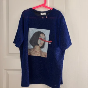 Blå glittrig t-shirt med konsttryck - Snygg blå glittrig t-shirt från X_T med ett stort konstnärligt tryck. T-shirten är transparent/mesh och har korta ärmar samt rund hals med metallöglor.