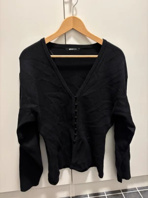 Svart kofta med v-ringning - Svart kofta från Gina Tricot med djup v-ringning och dekorativa knappar framtill. 