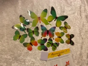 12st Dekoration Fjärilar  - Bilden visar ett set med färgglada 3D fjärilsdekorationer i plast, avsedda för väggmontering. Setet innehåller flera fjärilar i olika storlekar och färger samt självhäftande kuddar och instruktioner. Perfekt för att dekorera hemmet. Produkten ser oanvänd ut.