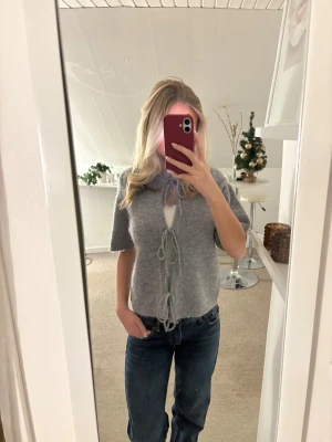 Grå kofta med knyt från Gina Tricot - Supermysig grå kofta från Gina Tricot i ullblandning. Kortärmad modell med tre knyt framtill och ribbade kanter. 