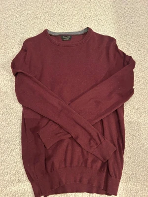 Vinröd tröja från Massimo Dutti - Snygg vinröd tröja från Massimo Dutti. Klassisk rund hals och långärmad modell med ribbade muddar. Perfekt att bära över en skjorta för en clean och stilren look.