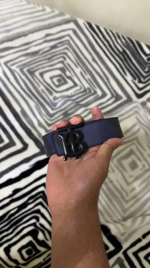 Rutmönstrat blått Burberry bälte - Snyggt bälte från Burberry med rutigt mönster i blått och svart. Bältet har en bred design och en cool svart metallspänne med Burberrys ikoniska B-logga. Och man kan vända den till andra sidan så bli den svart lite förstörd vid sista hålet. Ståg inte på den hur lång den va men mäte det så var den 115cm. Den är fejk