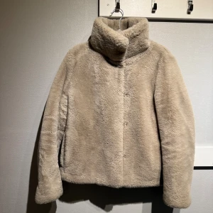 Beige pälsjacka från MNG XS - Supermjuk och fluffig kort fuskpälsjacka från Mango i beige färg. Jackan har hög krage, rak passform och är helfodrad med slät insida. Perfekt för kalla dagar när du vill vara både varm och snygg. Enkel och stilren design utan synliga detaljer framtill. Skick: Fint använt. Lite mer slitage vid ärmslut och lite vid fickor, men syns bara på riktigt nära håll. Går troligen att borsta till så syns det ännu mindre
