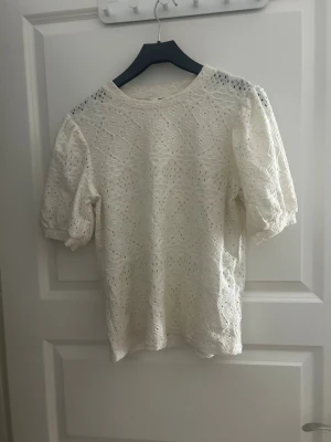Vit spetsblus med puffärm - Säljer en vit blus med korta puffärmar och rund hals. Blusen har ett detaljerat spetsmönster och är tillverkad i bomull. 