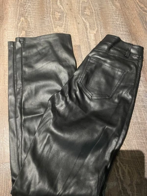 Svarta skinnbyxor från Bik Bok, strl 34 - Snygga fodrade  svarta skinnbyxor från Bik Bok i storlek 34. Byxorna har klassisk femficksdesign, raka ben och är tillverkade i mjukt syntetmaterial med skinnlook. Perfekta för dig som vill ha en edgy och trendig stil.