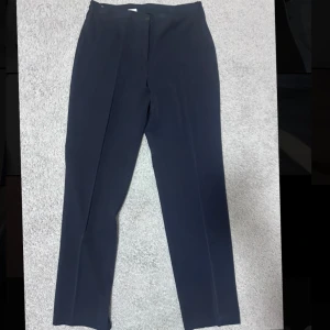  kostymbyxor med pressveck - Snygga svarta/marinblåa kostymbyxor med klassiskt pressveck och rak passform. Byxorna har en stilren look och är tillverkade i ett slätt tyg som ger en dressad känsla. Perfekta för dig som gillar en clean och tidlös stil.